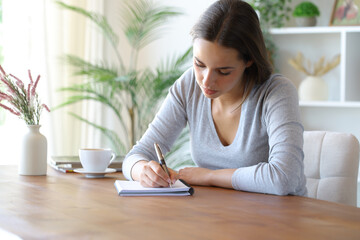 Woman taking notes in notebook on a wooden table in a room