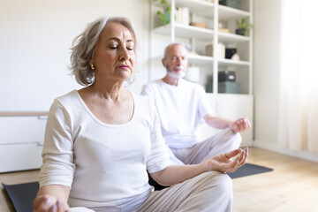 Senior couple meditating together at home, practicing yoga and mindfulness in comfortable clothes