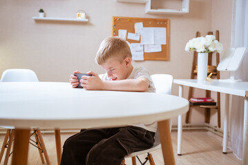 Fototapeta premium A boy with hearing aids engages with a smartphone, playing mobile games with focused enjoyment. Captures modern childhood, adaptive technology, and inclusive digital play
