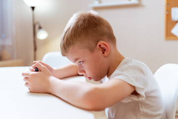 A boy with hearing aids engages with a smartphone, playing mobile games with focused enjoyment....