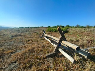 Low-angle view of metal pipe structure on dry grassy field under clear blue sky. Ideal for military, outdoor, rural, or environmental contrast-themed visual content