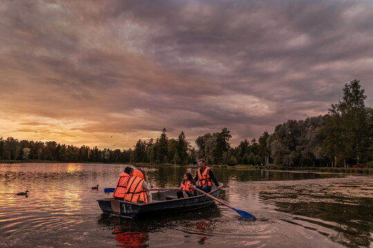 Man and three girls rowing a boat on a lake at sunset.