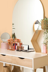Makeup table with cosmetics and mirrors near beige wall in dressing room