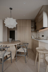 Open concept living and kitchen space featuring a wooden dining table, stylish chairs, and a chic pendant light. A seamless blend of natural wood and sleek modern elements.