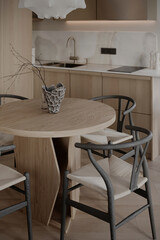 Modern dining area with a round wooden table, unique vase, and stylish chairs, paired with a sleek kitchen background.