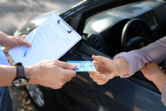 Male instructor giving driving license to examiner outdoors, closeup