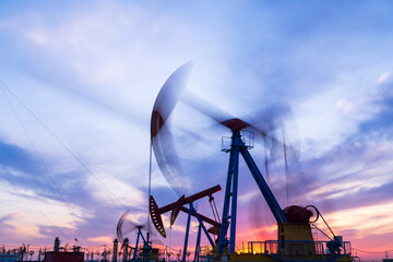 in the evening, oil pumps are running, The oil pump and the beautiful sunset reflected in the water, the silhouette of the beam pumping unit in the evening.