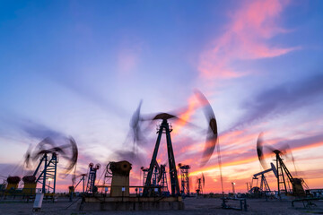 in the evening, oil pumps are running, The oil pump and the beautiful sunset reflected in the water, the silhouette of the beam pumping unit in the evening.