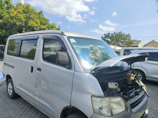 Silver van with open hood and front-end damage parked outdoors. Ideal for automotive, accident, inspection, or repair-themed visual content