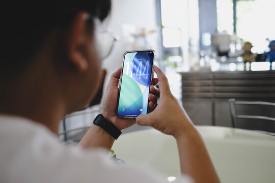 Bangkok, Thailand. September 22, 2025; A person looking at the time on the lock screen of their Apple iPhone, displaying the modern iOS 26 interface in a bright cafe.