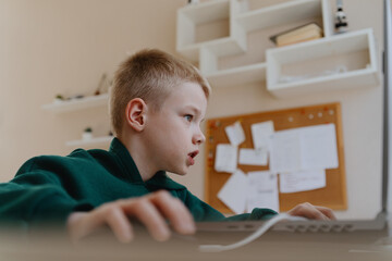A boy with hearing aids focuses intently while playing a game on his laptop, showcasing modern...