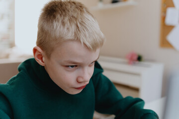 A boy with hearing aids focuses intently while playing a game on his laptop, showcasing modern...