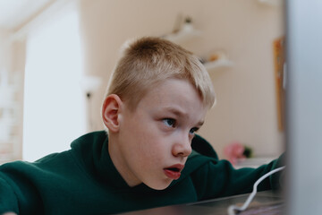 A boy with hearing aids focuses intently while playing a game on his laptop, showcasing modern...