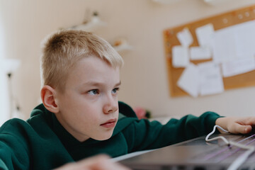 A boy with hearing aids focuses intently while playing a game on his laptop, showcasing modern...