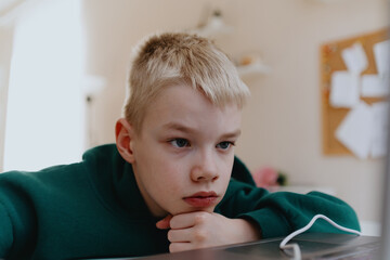 A boy with hearing aids focuses intently while playing a game on his laptop, showcasing modern...
