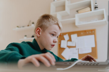 A boy with hearing aids focuses intently while playing a game on his laptop, showcasing modern...