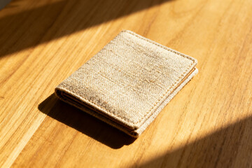 A beige textured wallet resting on a wooden surface illuminated by natural sunlight