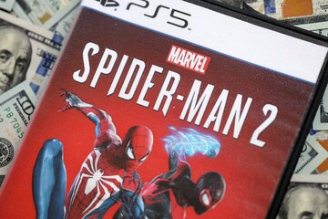 Naklejka premium KYIV, UKRAINE - SEPTEMBER 8, 2025 Marvels Spider-Man 2 videogame lies on big amount of hundred dollar bills