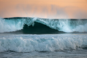 A powerful ocean wave rises under a soft pink and purple sunset sky at Bronte Beach, Sydney, Australia.
