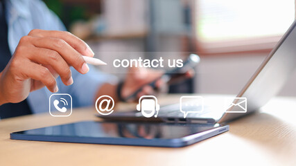 Business hand using digital pen on tablet with contact us icons: phone, email, chat, and support. Customer service, communication technology, and online business concept.