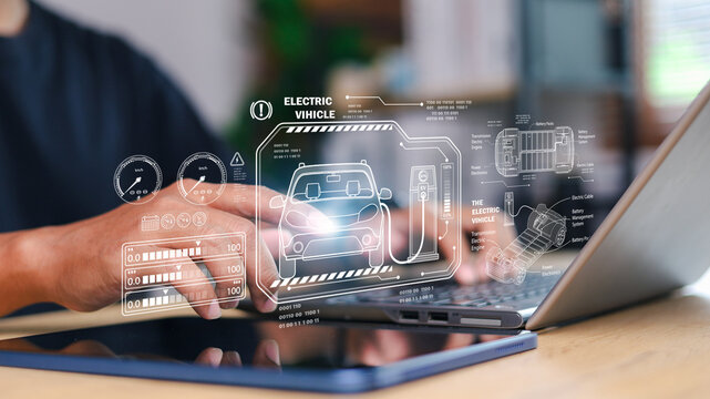 Hand using digital pen with laptop and tablet showing hologram interface of electric vehicle, battery management system, and charging technology for future mobility.