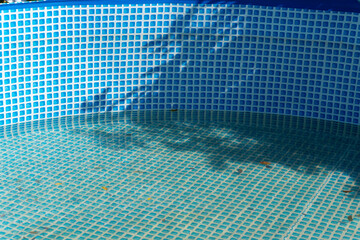 Sunlight and shadows fall across the blue-tiled wall of a pool. The water surface reflects subtle patterns.