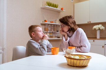 A boy with hearing aids and his mother share a warm conversation over tea in their cozy kitchen. A tender moment of family bonding, communication, and inclusive love