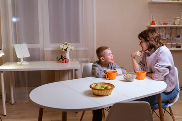 A boy with hearing aids and his mother share a warm conversation over tea in their cozy kitchen. A tender moment of family bonding, communication, and inclusive love