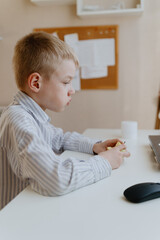 A boy with hearing aids in a button-down shirt enjoys a crisp apple at the kitchen counter. A natural moment of healthy snacking and inclusive childhood authenticity