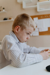 Fototapeta premium A boy with hearing aids in a button-down shirt enjoys a crisp apple at the kitchen counter. A natural moment of healthy snacking and inclusive childhood authenticity