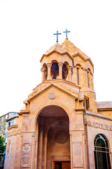 Beautiful close-up of a golden stone Armenian church in Yerevan, featuring twin towers with crosses, detailed carvings, and elegant arches. A striking example of Armenian Christian architecture