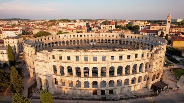4K aerial drone orbit around the Pula Arena, one of the best-preserved Roman amphitheaters in the world. Captured at golden hour, showing detailed architecture and surrounding cityscape. 