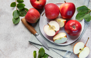 Fresh red apples whole and sliced on white plate with green leaves