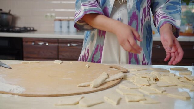 Woman in ethnic clothing preparing baursak dough pieces on wooden board