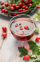 Steaming rosehip tea with fresh rose hips on rustic wooden table