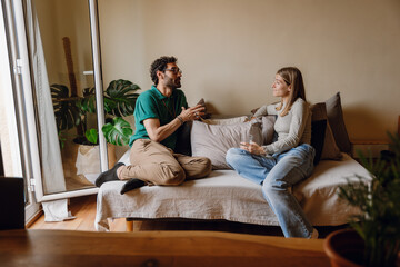 A man is talking to a woman sitting next to him on the couch while they hold glasses
