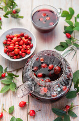 Steaming rosehip tea brewing in glass teapot with fresh rosehips