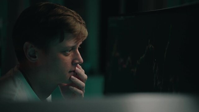 Pensive stressed stock trader studying financial charts on computer monitor, evaluating market trends with contemplative facial expression, fingers resting near lips in concentrated workspace, closeup