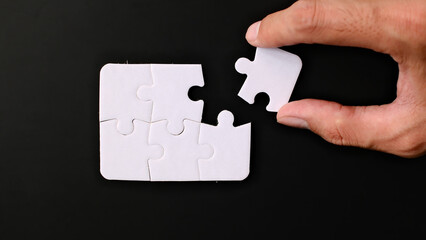 A hand connects puzzle pieces on a black background, completing a task or solving a problem