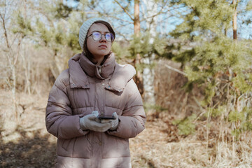 Fototapeta premium A young woman in a park uses her phone to navigate, enjoying nature while finding her way. Captures modern exploration, relaxation, and technology in daily life