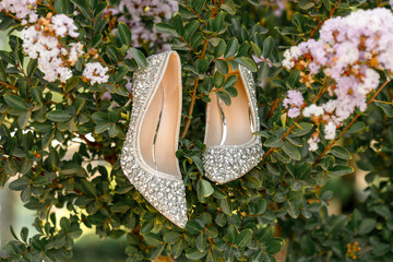 Sparkling silver high heels with rhinestone embellishments displayed on a blooming shrub. Elegant...