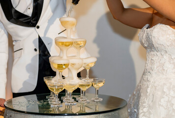 Bride and groom pour bubbly champagne into a tower of glassesNewlyweds pour sparkling wine over the top into a tower of glasses. Bride and groom pour bubbly champagne into a cascade of glasses at a we