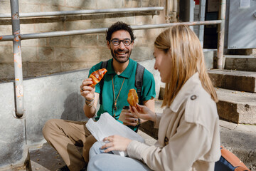 A man and a woman sit on the stairs and laugh while holding croissants