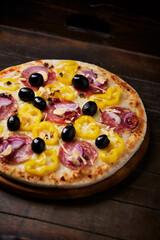 Pizza with salami, mozzarella cheese, black olives and pepper. Rustic wooden background. Soft focus. Copy space.	