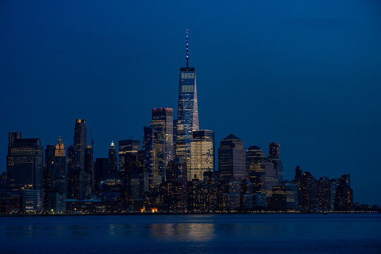 Fototapeta View of city skyline with towering skyscrapers reflecting the fading light of dusk over the tranquil water, New York, New York, United States.