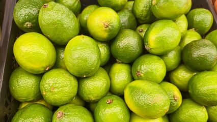 Green limes in large crates on store shelves. Display and sale of citrus fruits.