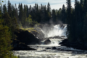 Ristafallet waterfall, Indalsälven river, in Jämtland, Sweden. 14 metres high natural powerful water energy, green forest and blue sky.