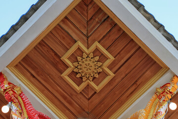 Traditional wooden ceiling with intricate golden floral carvings and symmetrical geometric frames in temple architecture.
