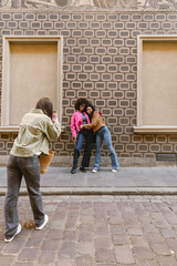 Fototapeta premium Two female friends hugging and posing while smiling and looking at the phone held by the female friend standing across from them