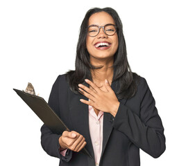 Latina businesswoman holding a report laughs out loudly keeping hand on chest.